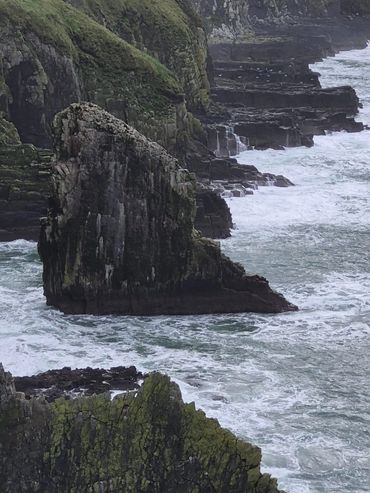 Rugged sea cliffs with waves crashing against them under overcast skies.