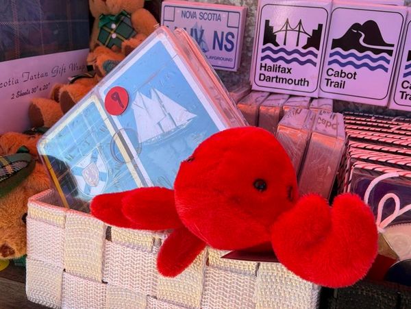 A red plush lobster toy in a basket with Nova Scotia souvenirs.