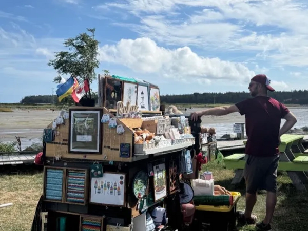 A man stands beside a seaside souvenir stall under a clear sky.