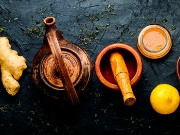 Rustic kitchen setup with ginger, lemon, honey, and wooden tools on a dark surface.