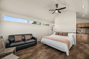 Modern studio with a cozy bed, black leather sofa, and wooden kitchen area.