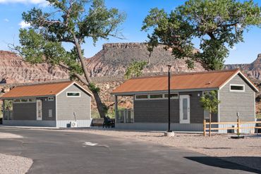 Two gray cabins with rusty roofs under trees near rocky cliffs.