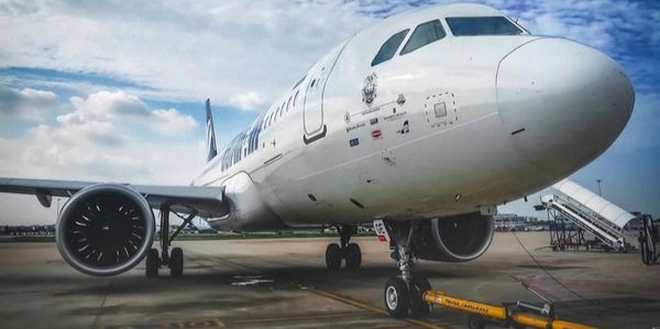 White commercial airplane parked on the tarmac under a partly cloudy sky.