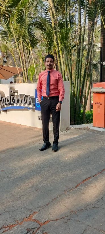 Man in formal attire standing near Radisson hotel sign with greenery in the background.