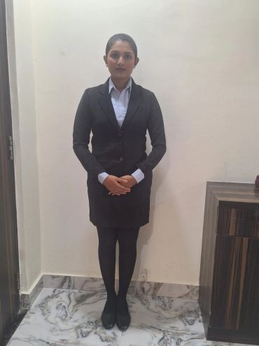 Woman in formal black suit standing with hands clasped in a marble-floored room.