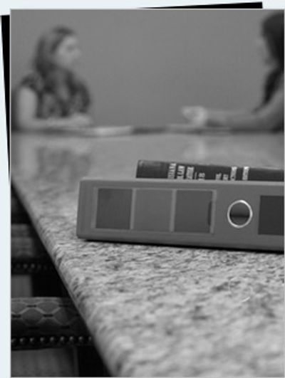 A binder on a conference table with two people blurred in the background.