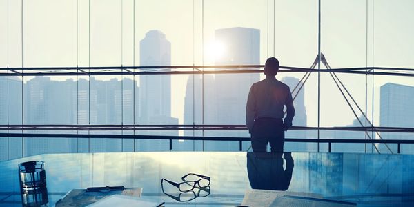 Businessman gazing out office window at city skyline during sunrise.