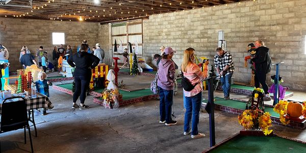 Indoor miniature golf game with people playing and watching.