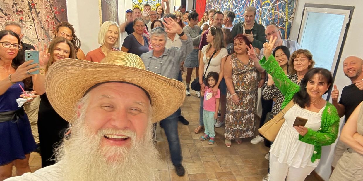 A joyful group selfie with a man in a straw hat and a lively crowd behind him.
