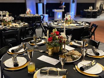 Guest tables at a wedding reception, covered with black tablecloths, gold and white place settings.