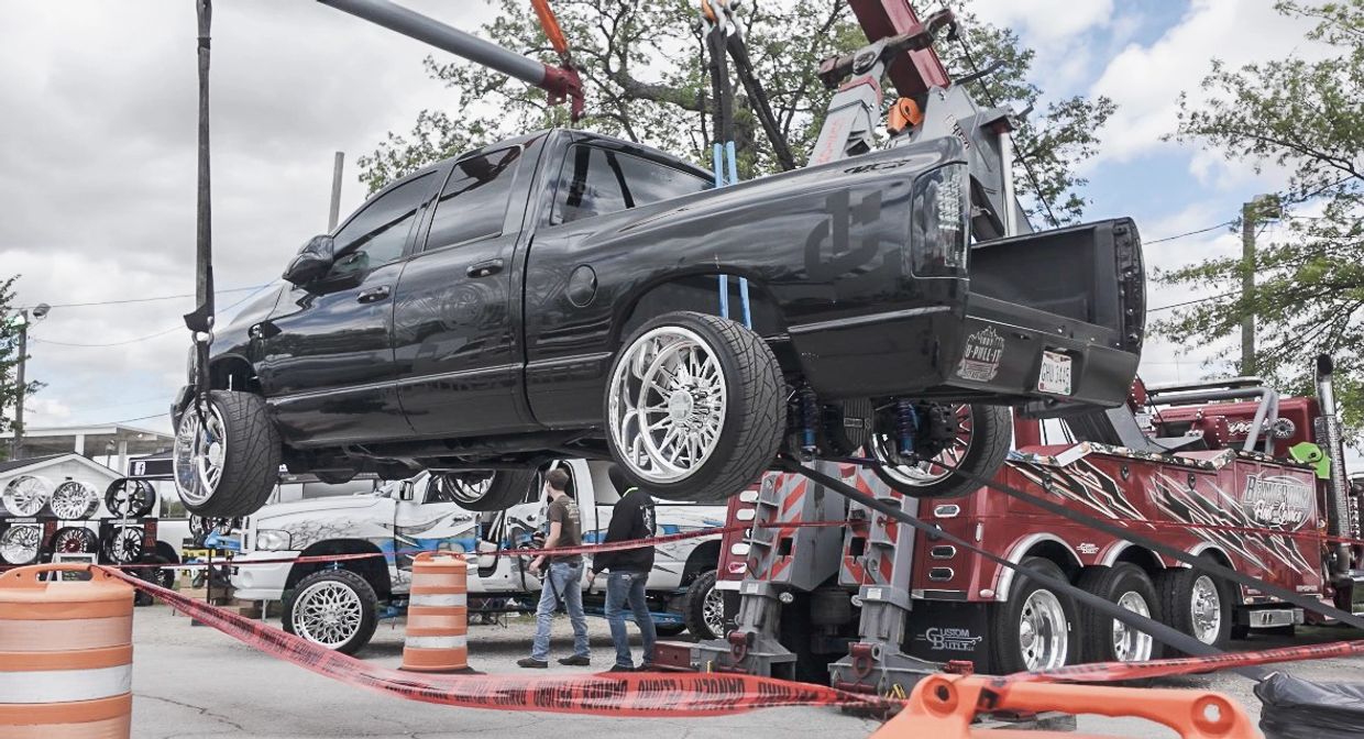 A black pickup truck lifted by a crane at a car show.