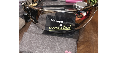 A reflective bowl with makeup products and a sticker saying 'Makeup is overrated'.