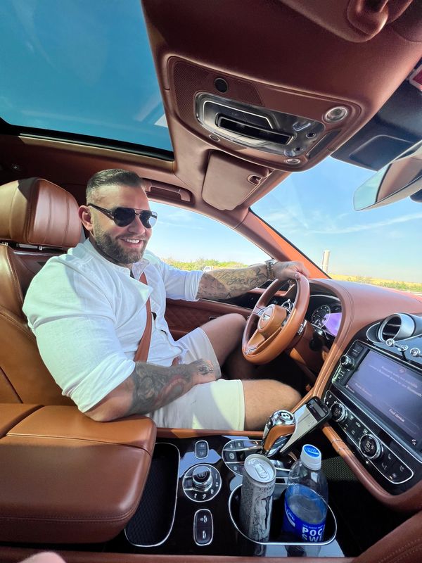 Andy Lee driving a luxury car with tan leather interior, wearing sunglasses and a white shirt