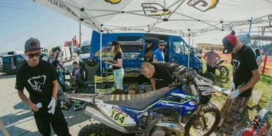Motocross team prepares bike under tent at outdoor event.