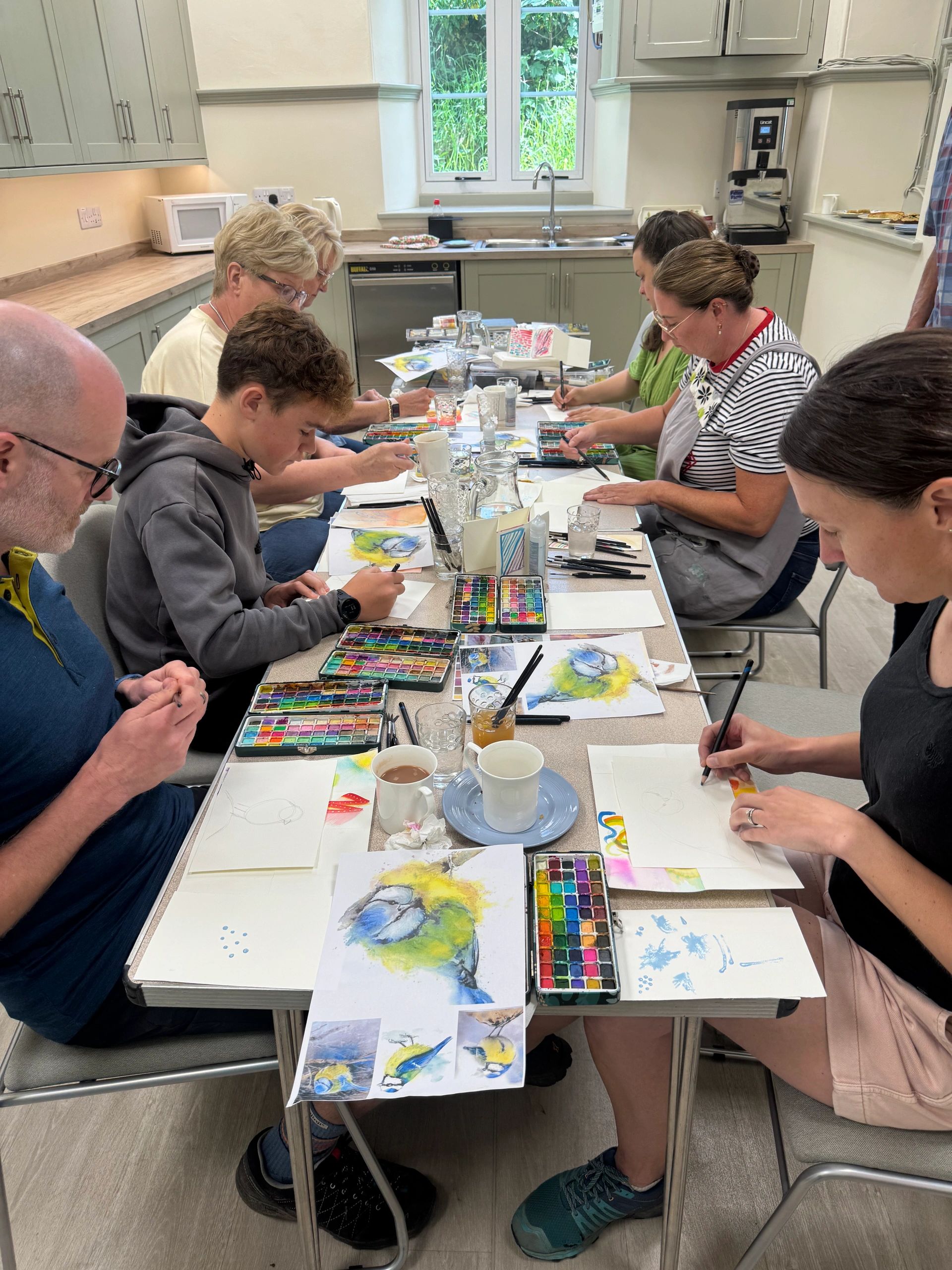 Group painting class with watercolor bird artwork in a bright kitchen.