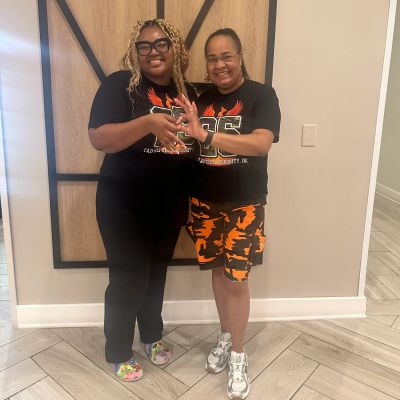 Two women smiling, holding hands indoors.