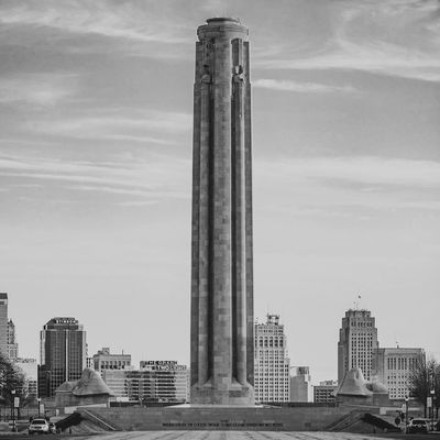 Tall stone monument in an urban setting with skyscrapers in the background.