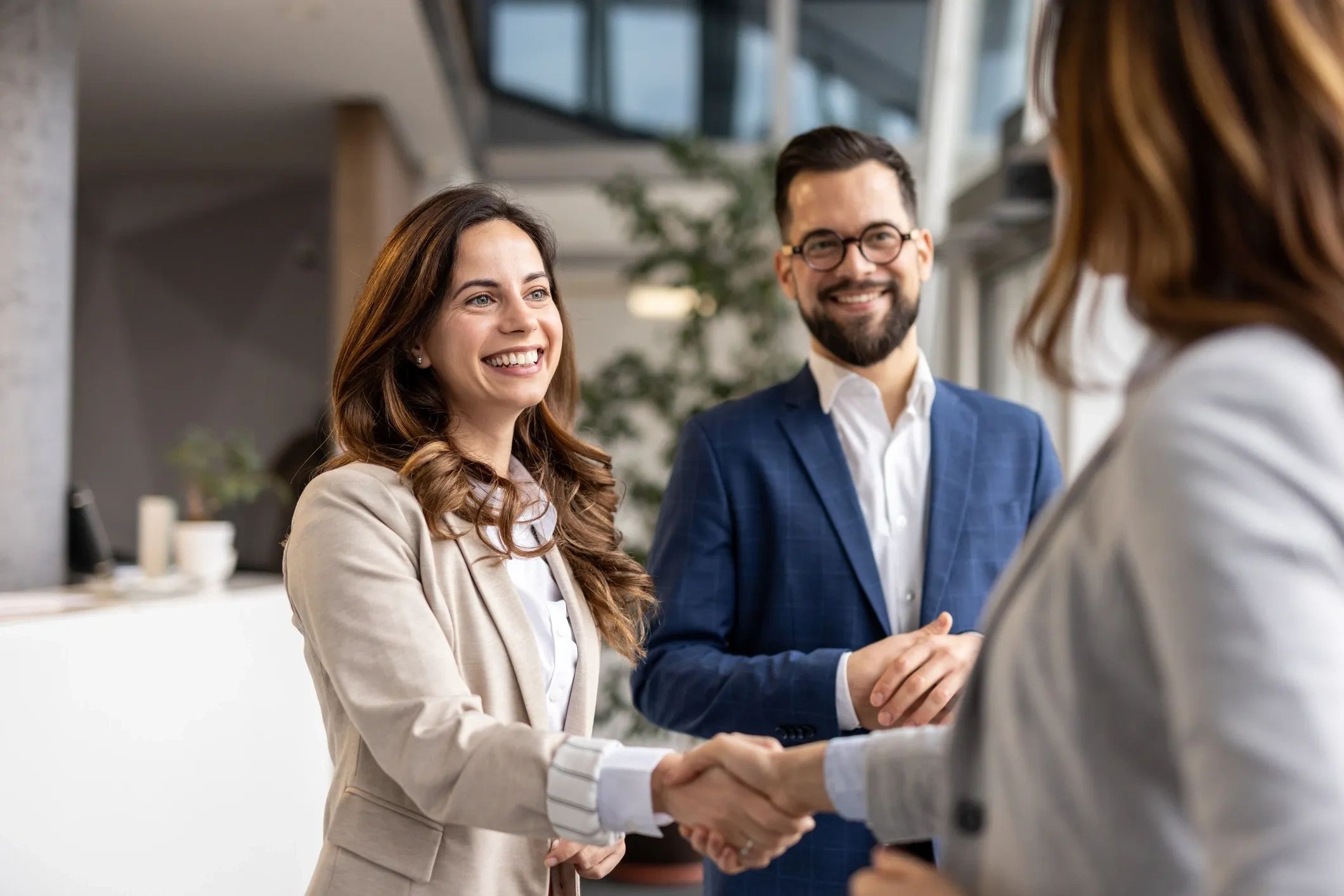 Two professionals shaking hands with a smiling man watching.