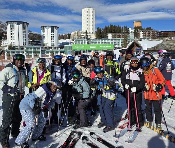 Group of skiers posing happily on snowy slopes with buildings in the background.