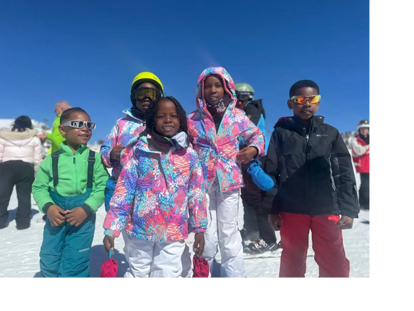 A group of kids in colorful ski outfits posing on a snowy mountain under a clear blue sky.