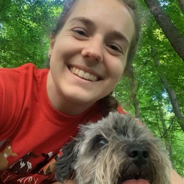 Smiling woman with her dog outdoors in a forested area.