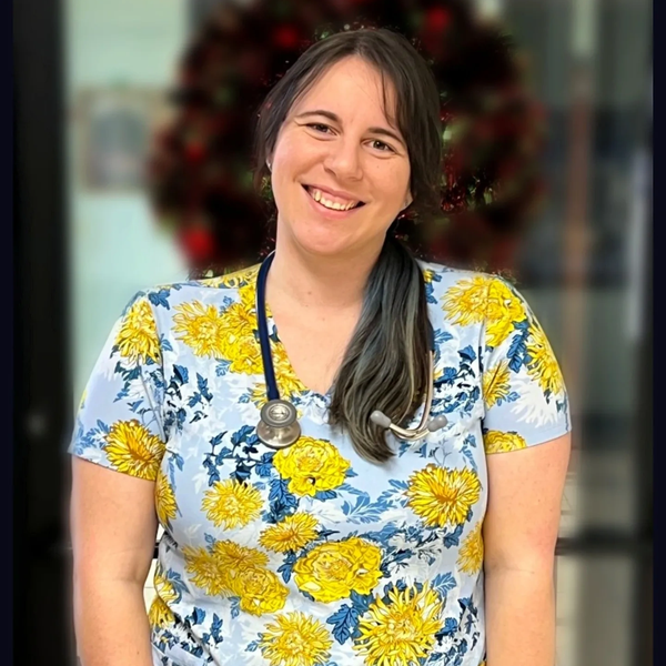 Smiling female healthcare worker in floral scrubs with stethoscope.