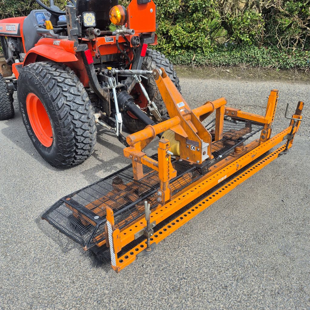 Orange Kubota tractor with an attached ground leveling implement on a paved road.