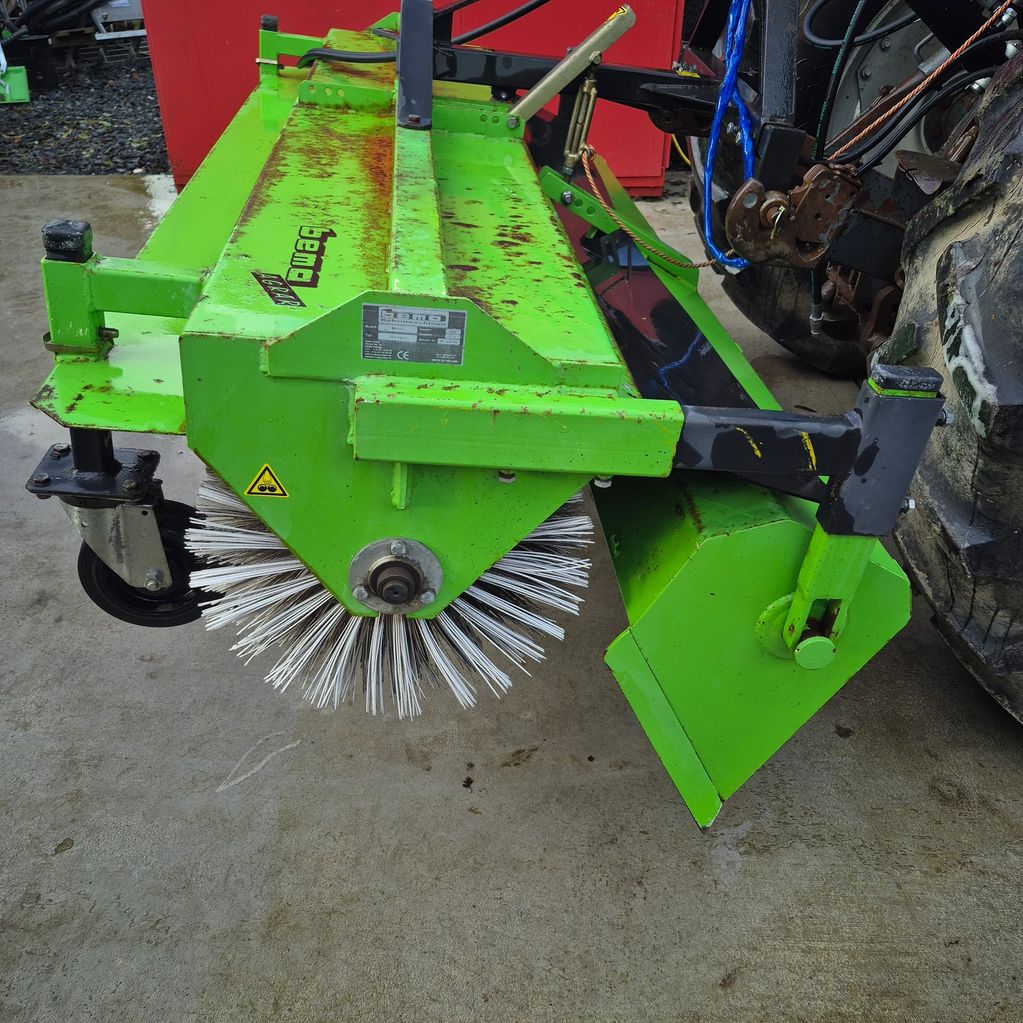 Green industrial rotary brush attachment on a tractor for cleaning surfaces.