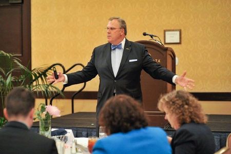 Roger Rickard with his arms wide open while presenting to an audience.