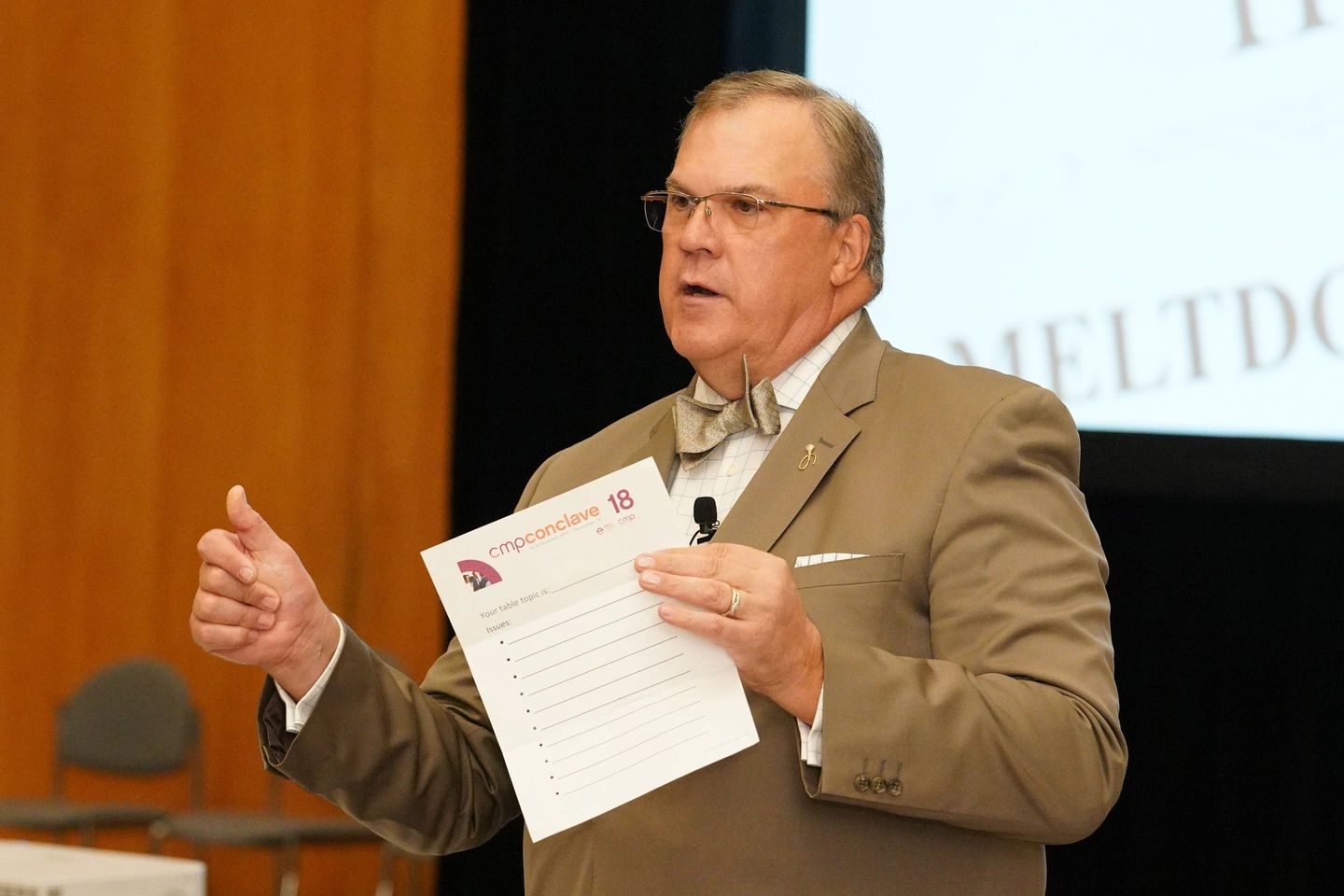 Man in a suit holding a paper and speaking at an event.