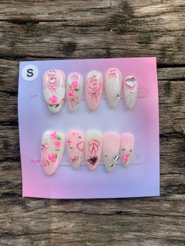 Pink-themed press-on nails with roses, bows, and rhinestone accents.