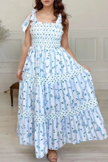 Woman in a white and blue floral maxi dress holding the skirt.