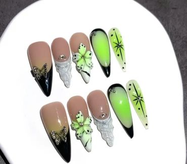Elegant stiletto nails with butterfly, flower, and green gradient designs.