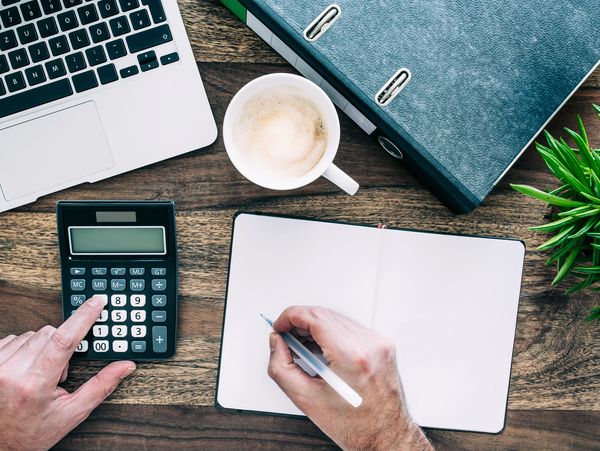 Top view of person at desk using calculator while taking notes