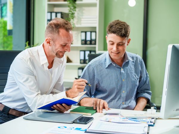 An Italian male and a Caucasian male sit at business desk in office meeting room