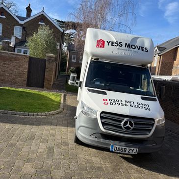 A white Mercedes moving truck parked on a residential driveway under a blue sky.