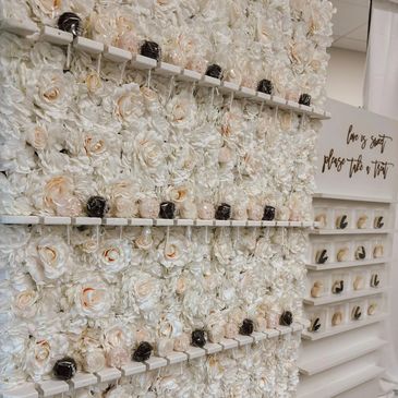 White, floral wall with inserts and brown, pink, and white cake pops inside. Beside is another white
