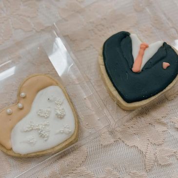 Heart shaped sugar cookies, one that resembles a wedding dress with pearl sprinkles. The other one a