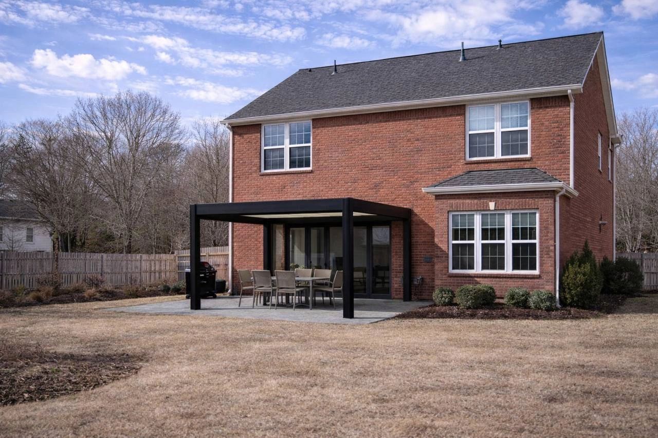 Modern black aluminum pergola installed in a backyard patio behind a red brick house.