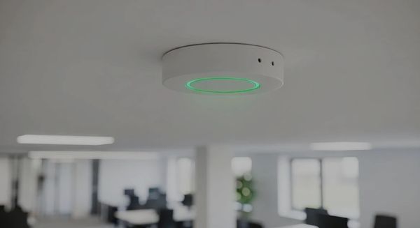 White ceiling-mounted wireless access point with a green status light in an office