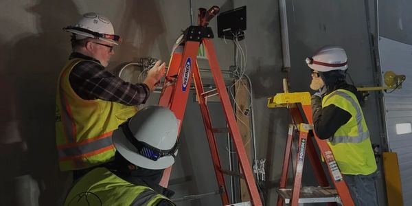 Three individuals wearing hard hats and pulling structured cabling