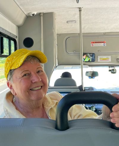 Smiling woman with yellow cap sitting on a bus.
