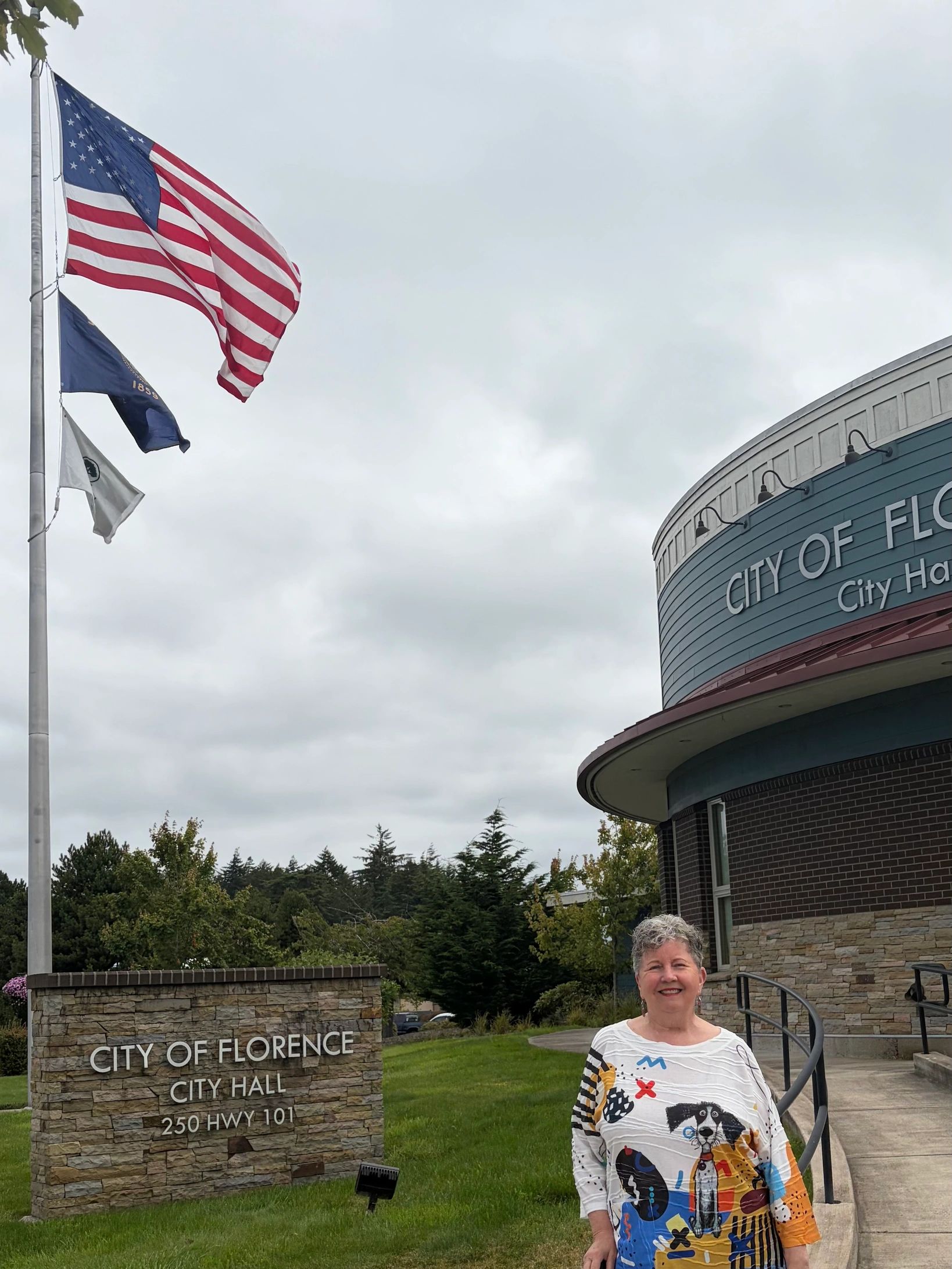 Woman standing near City of Florence City Hall sign with flags flying.