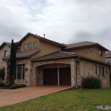A modern house with stone and stucco walls, brown roof, wooden garage doors, and a manicured lawn.