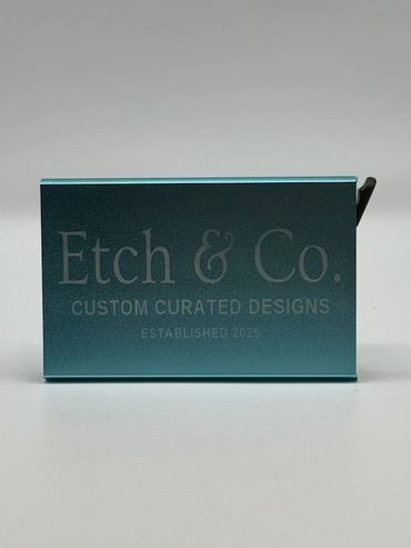 A teal rectangular box with 'Etch & Co. Custom Curated Designs Established 2025' engraved on it.