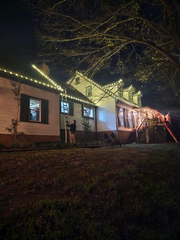 A man sets up holiday lights on a house at night.