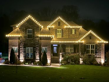 A large house illuminated with warm string lights outlining the roof at night.