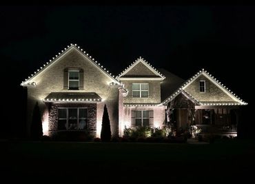 A beautifully lit brick house at night with white roofline lights.