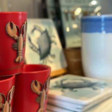 Ceramic lobster-themed red cups and crab-printed coasters on a shelf.
