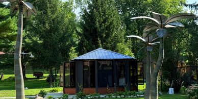 Metal palm tree sculptures and a small pavilion in a green garden.